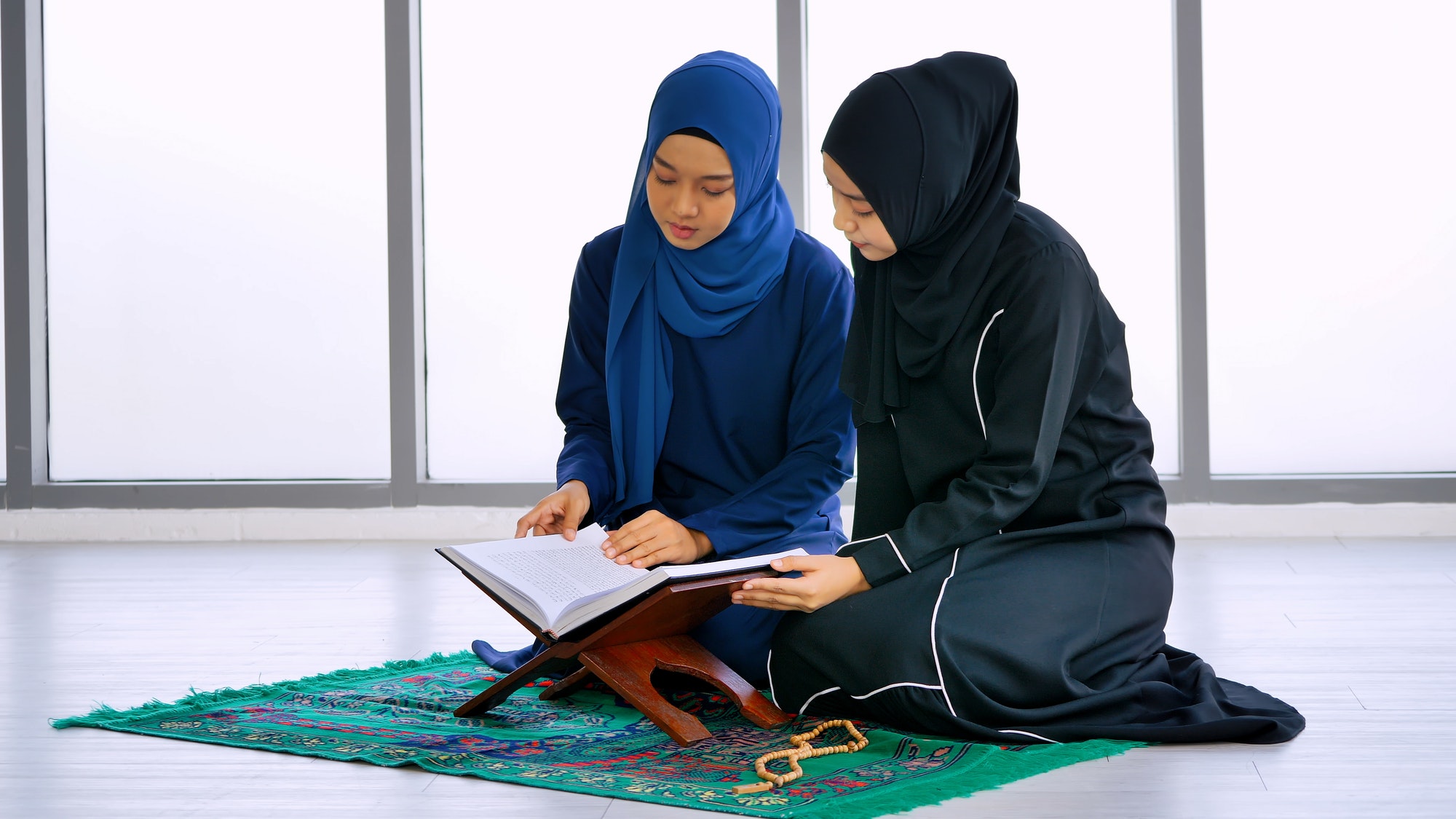 Two Muslim Asian women wearing traditional hijab are reciting prayers in the Quran. Two Muslim Asian women wearing traditional hijab are reciting prayers in the Quran.